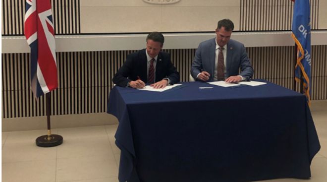 Kevin Stitt and Nigel Huddleston sign the MOU